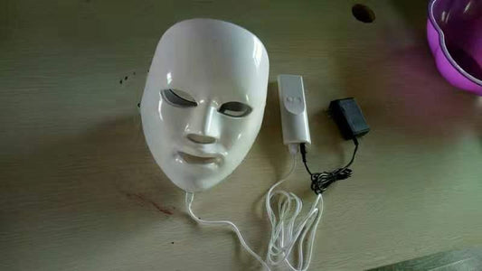 white LED light therapy facial mask with remote control and power adapter on wooden surface